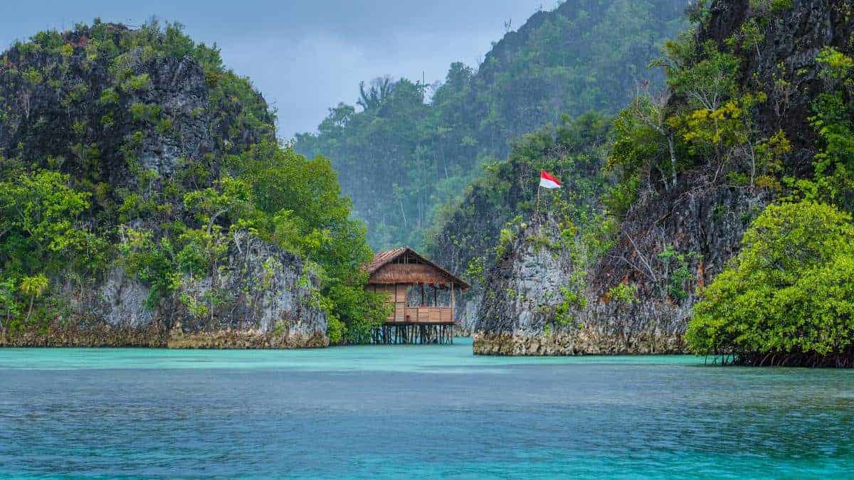 Bamboo Hut between some Rocks under Rain in Bay with Indonesian Flag, Pianemo Islands, Raja Ampat